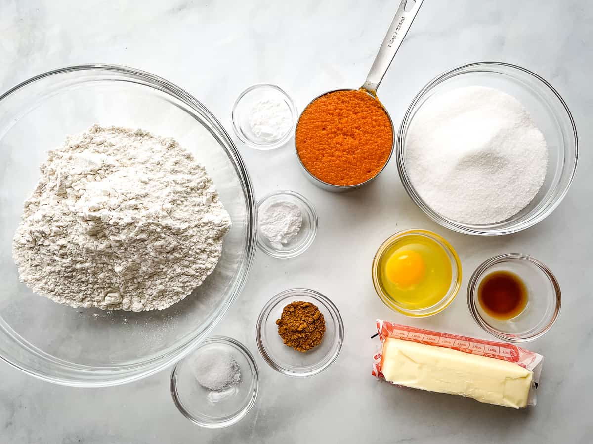 Ingredients for gluten-free pumpkin cookies in individual bowls and measuring cups. A stick of butter sits on a wrapper.
