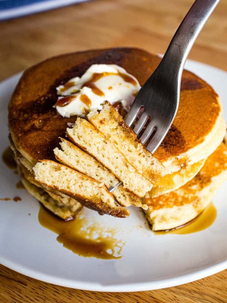 Forkful of almond flour pancakes above a stack of pancakes with butter and syrup.