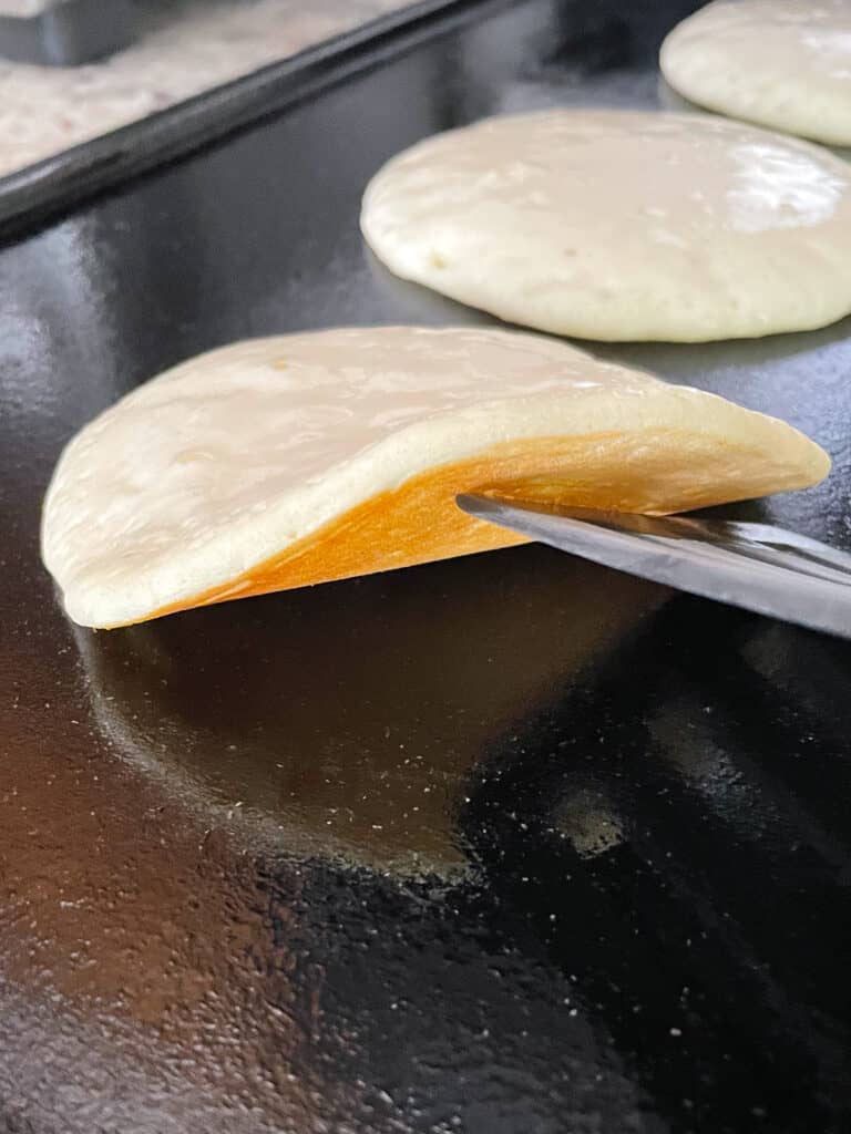 Lifting edge of pancake with a spatula on a griddle to check for doneness.