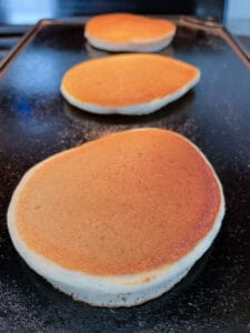Three gluten-free pancakes on a griddle.