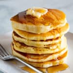 Stack of gluten-free pancakes on a plate with butter and syrup.