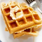 Stack of gluten-free waffles with butter and syrup on a plate.