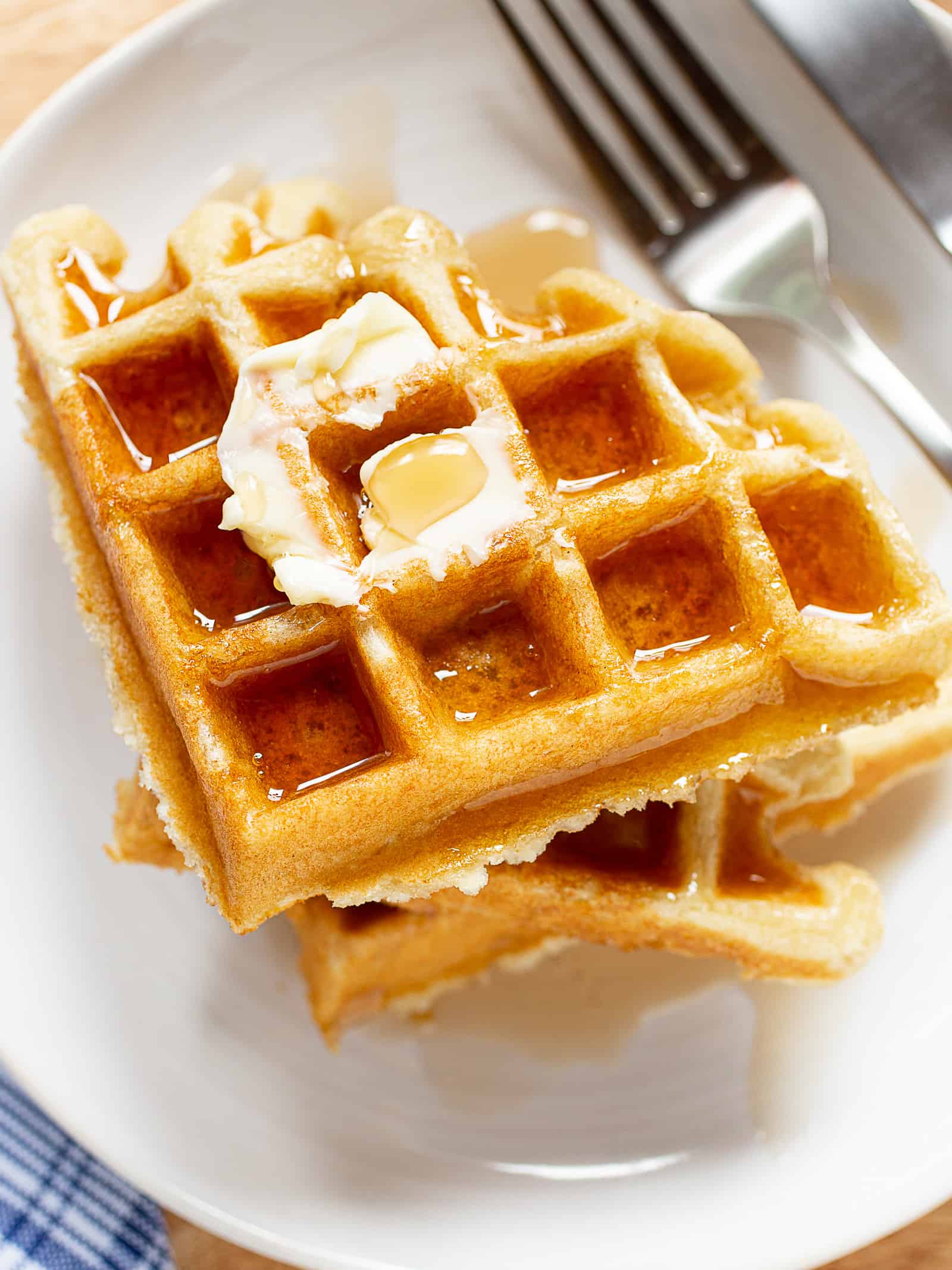 Stack of gluten-free waffles with butter and syrup on a plate.
