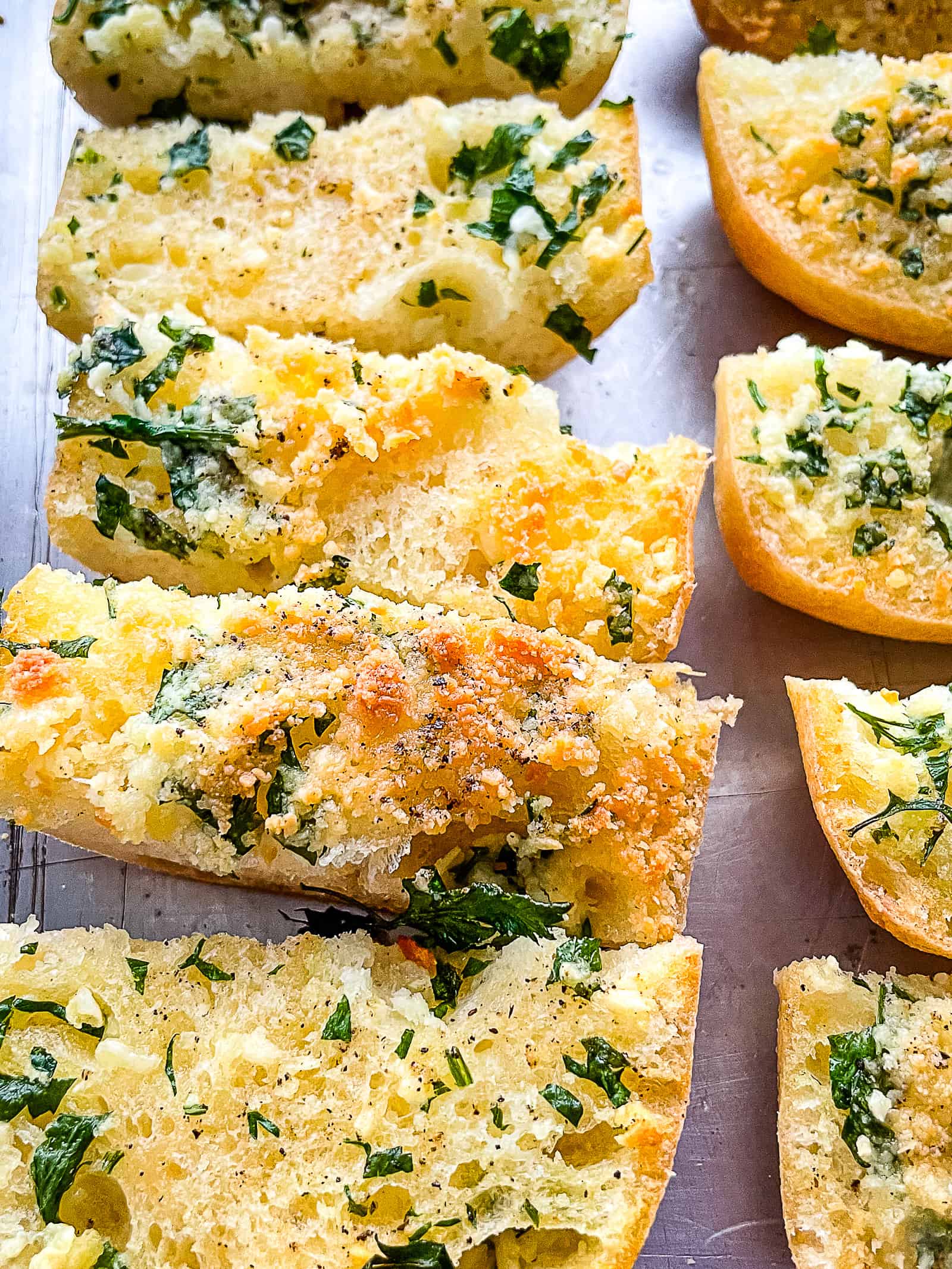 Slices of baked gluten-free garlic bread on a sheet pan.
