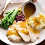 Pouring gluten-free gravy on turkey on a Thanksgiving plate.