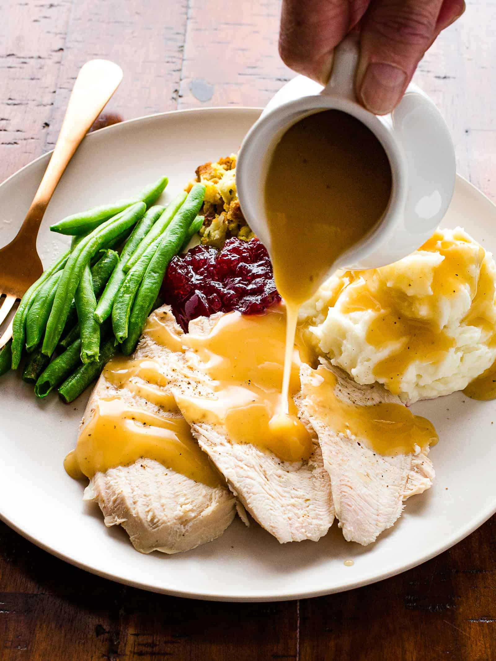 Pouring gluten-free gravy on turkey on a Thanksgiving plate.