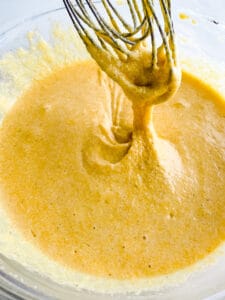 Gluten-free cornbread batter in bowl and falling off a whisk.