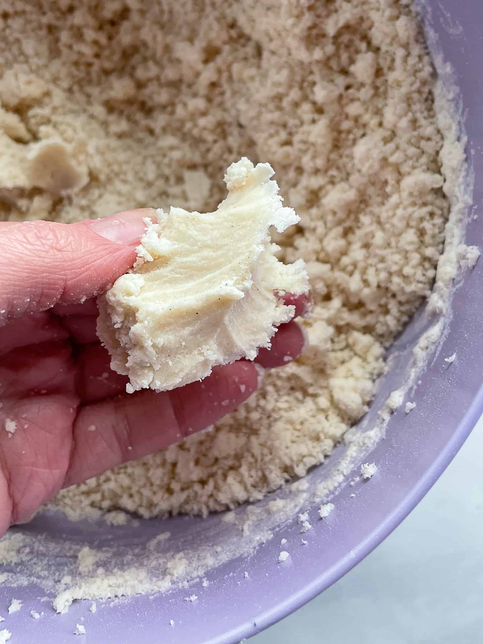 Gluten-free shortbread dough pressed into a small ball. Crumbly dough is in a bowl in the background.