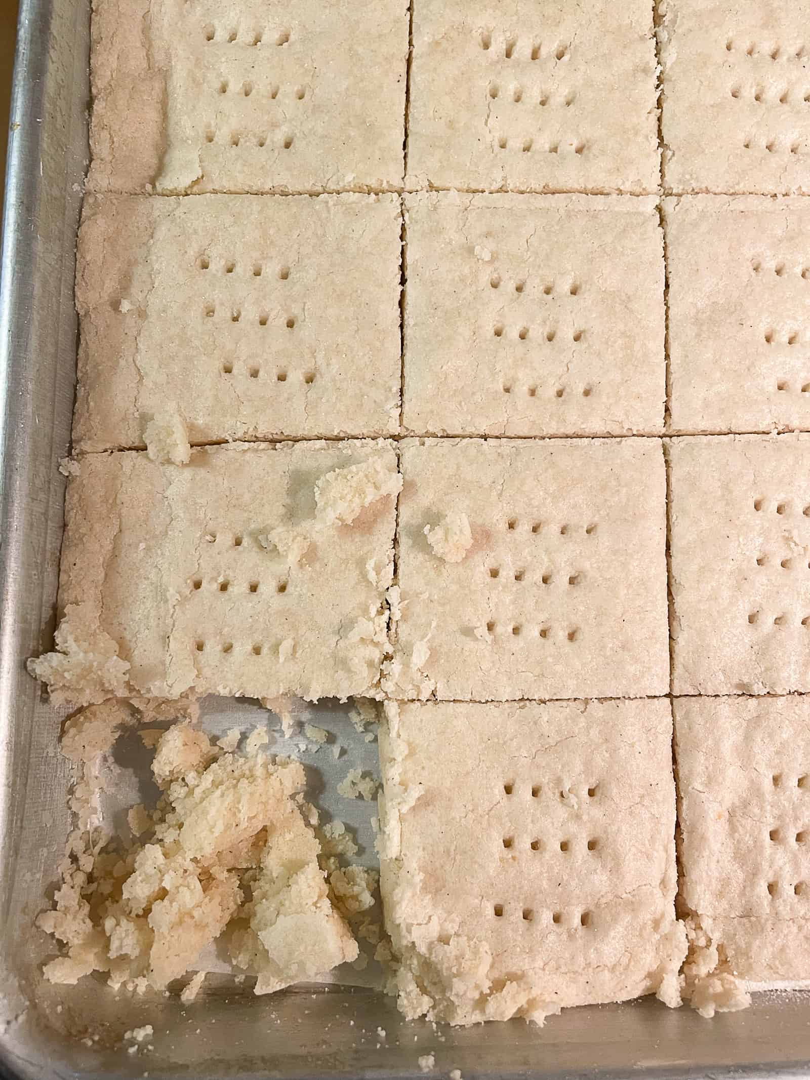 Gluten-free shortbread cookie in a pan. Lower left cookie crumbled because it was cut when hot.