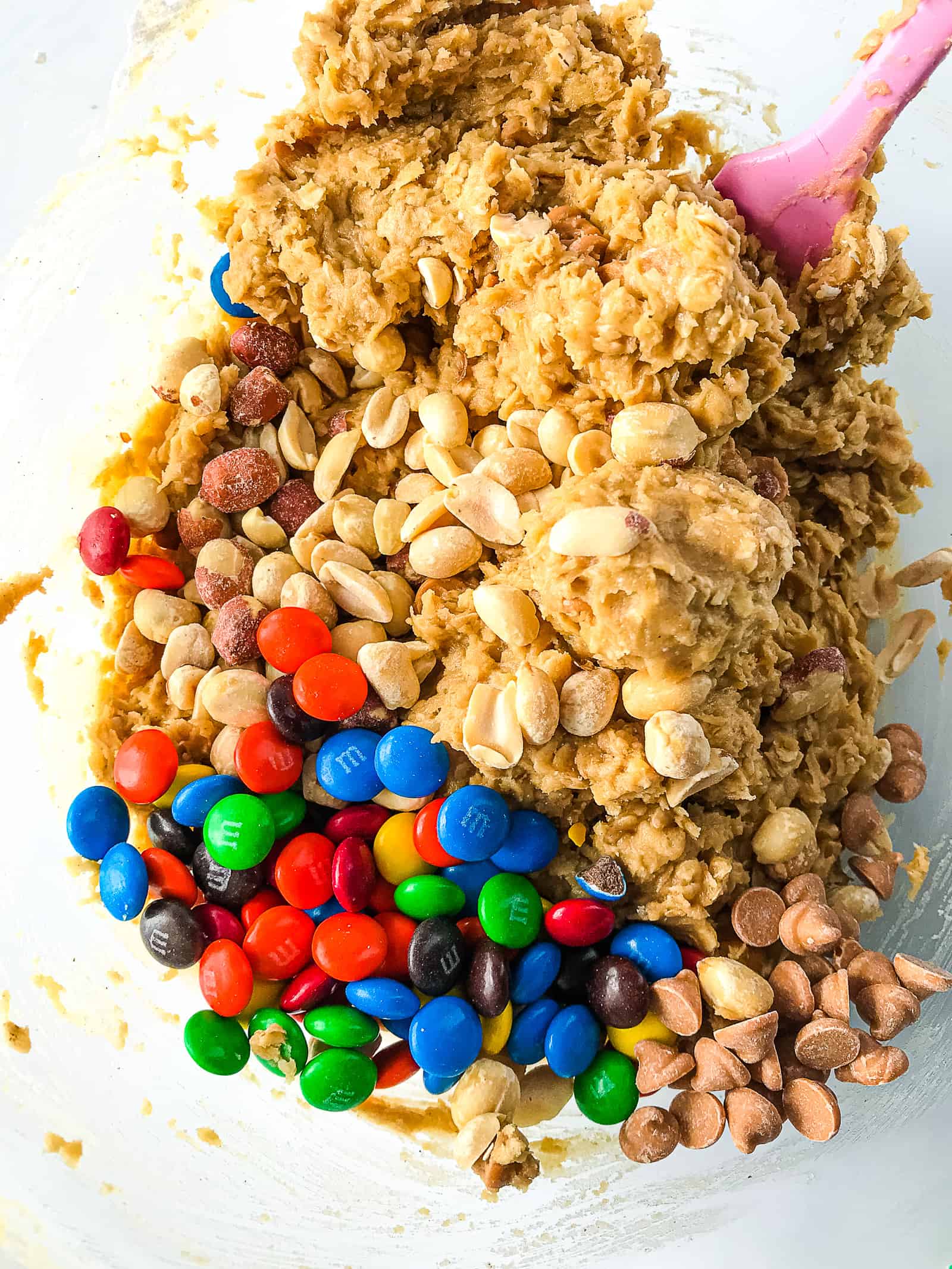 Mxing M&Ms, peanuts, and butterscotch chips into gluten-free monster cookie dough.