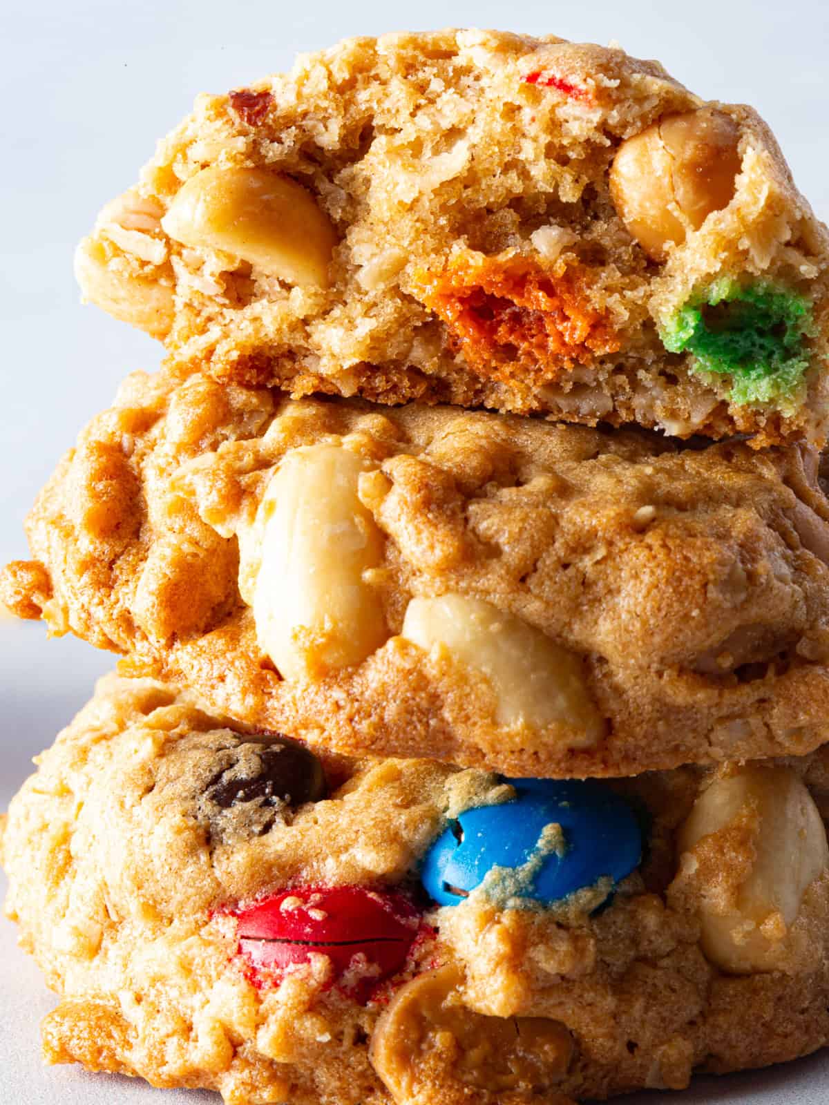 Stack of three gluten-free monster cookies. The top cookie is broken in half.