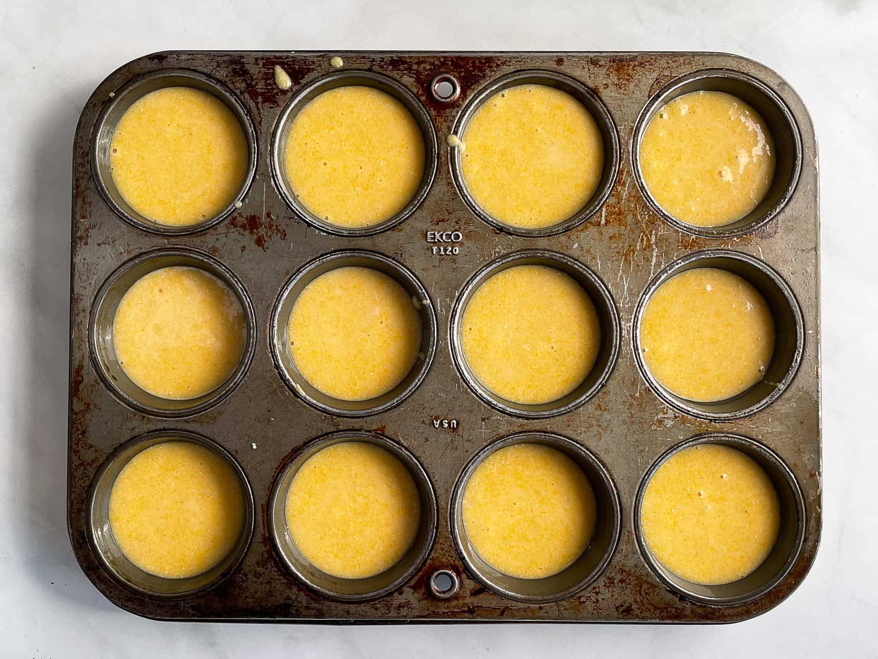 Gluten-free corn muffin batter in an old, greased muffin pan.
