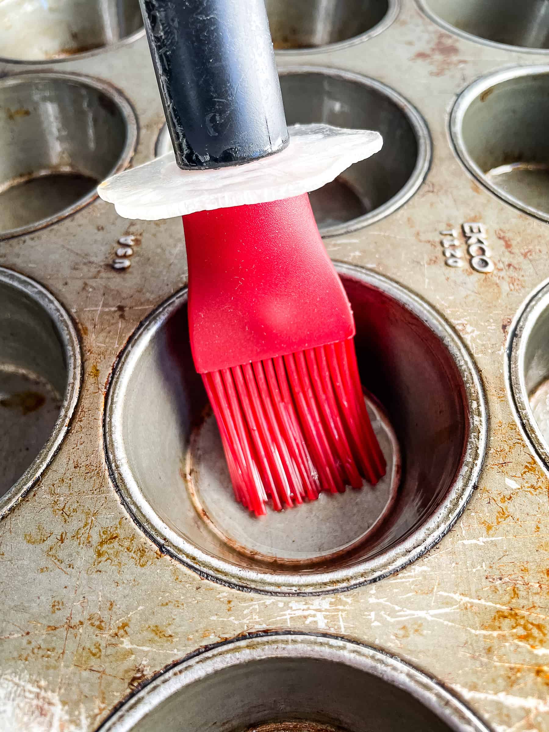 Greasing a nonstick muffin pan with a red silicone spatula. Muffin pan is old.