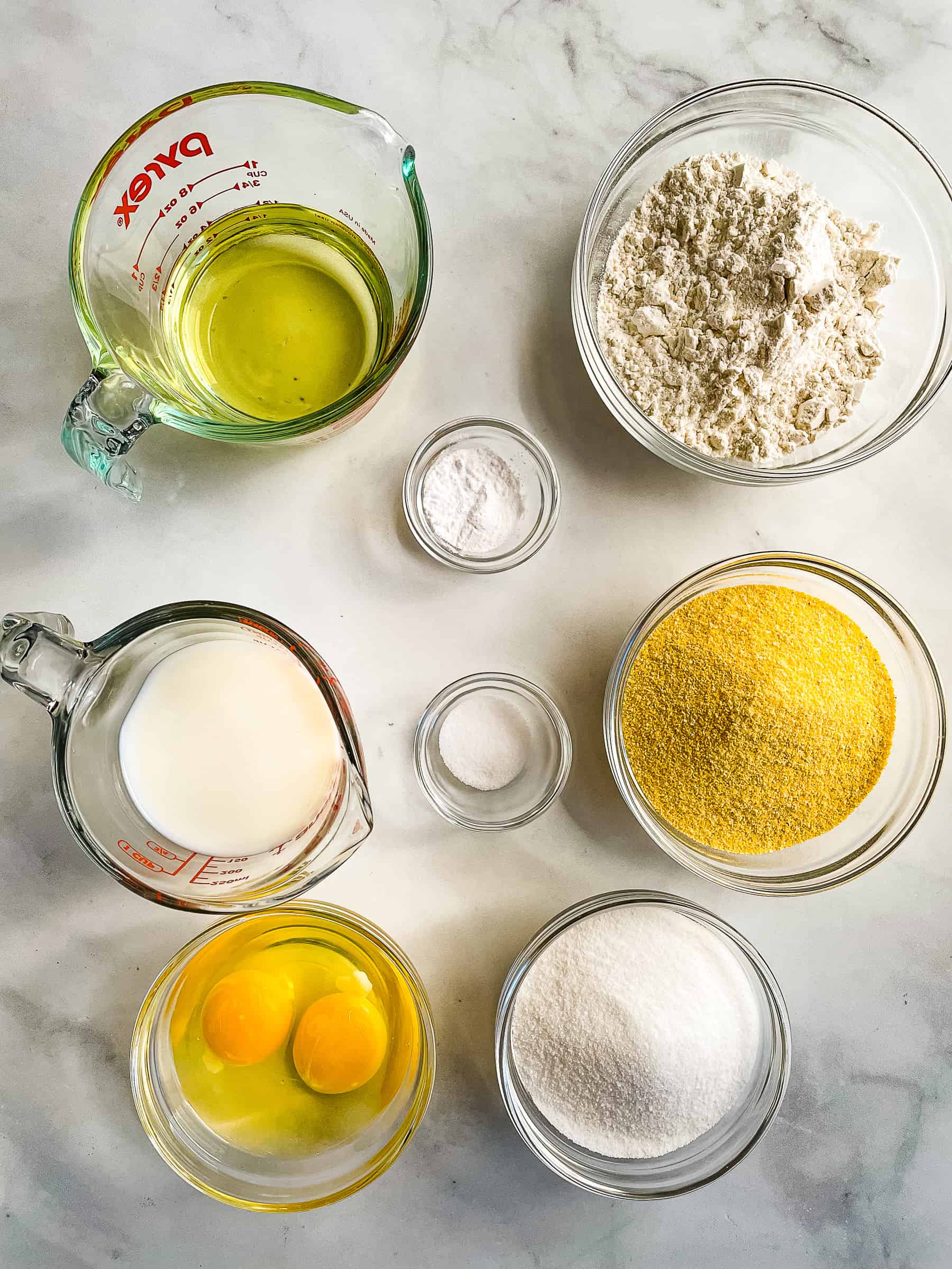 Ingredients for gluten-free corn muffins in individual bowls and measuring cups on a counter.