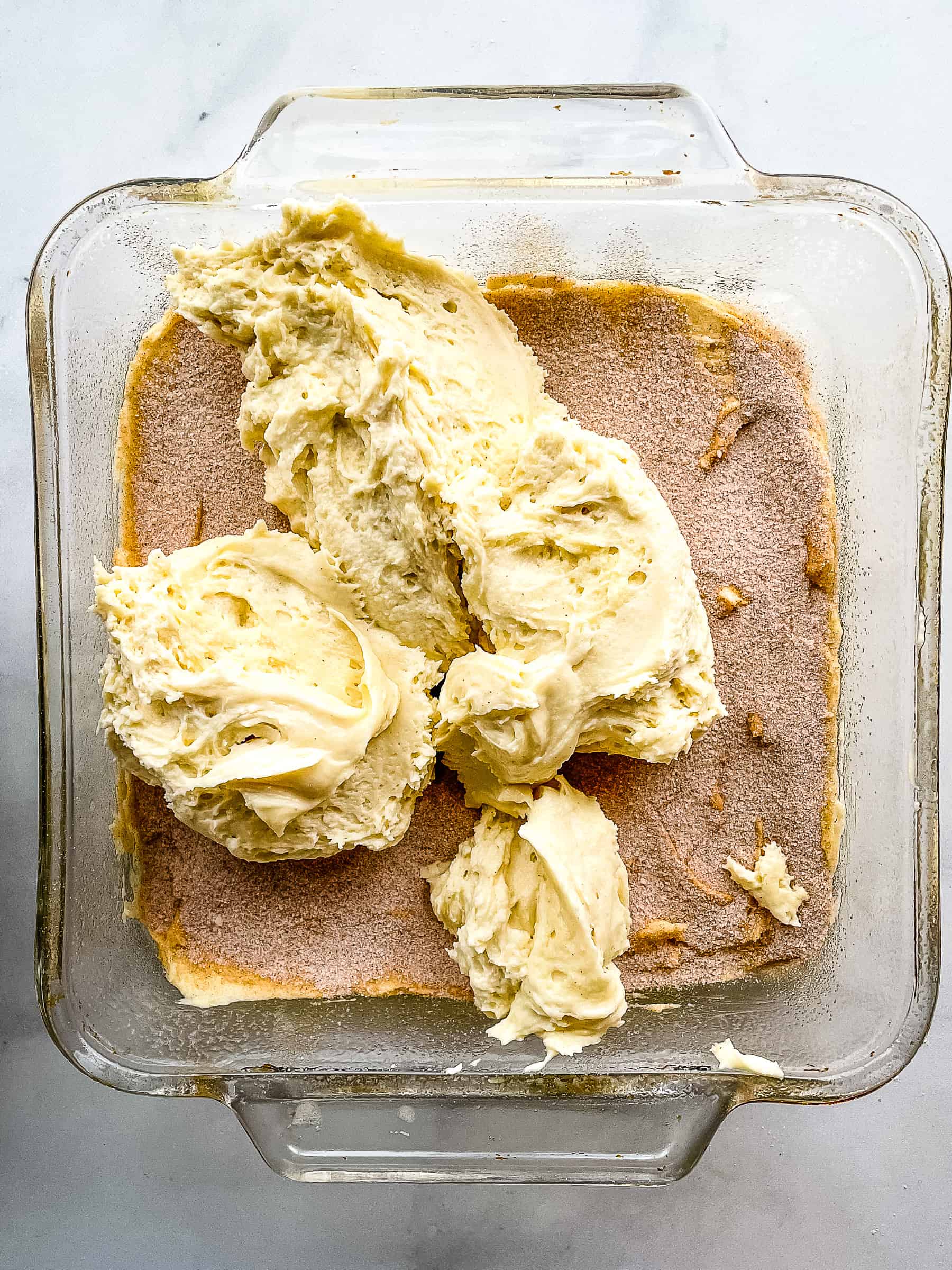 Gluten-free coffee cake batter in a pan with cinnamon sugar filling. A layer of batter is about to be spread over the filling.