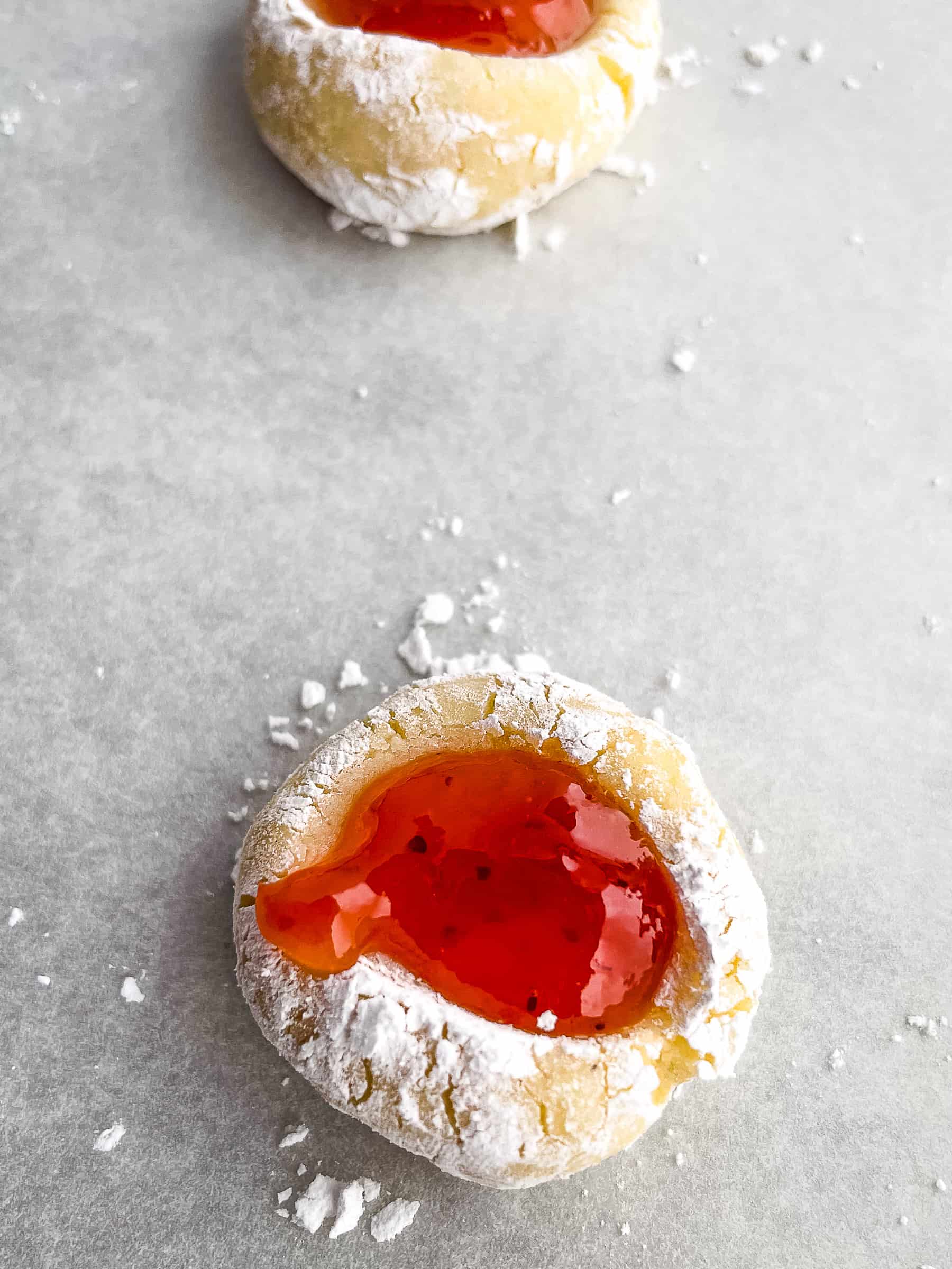 Unbaked gluten-free thumbprint cookie with jam and powdered sugar on baking sheet.