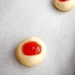 Unbaked gluten-free thumbprint cookies topped with strawberry jam on a baking sheet.