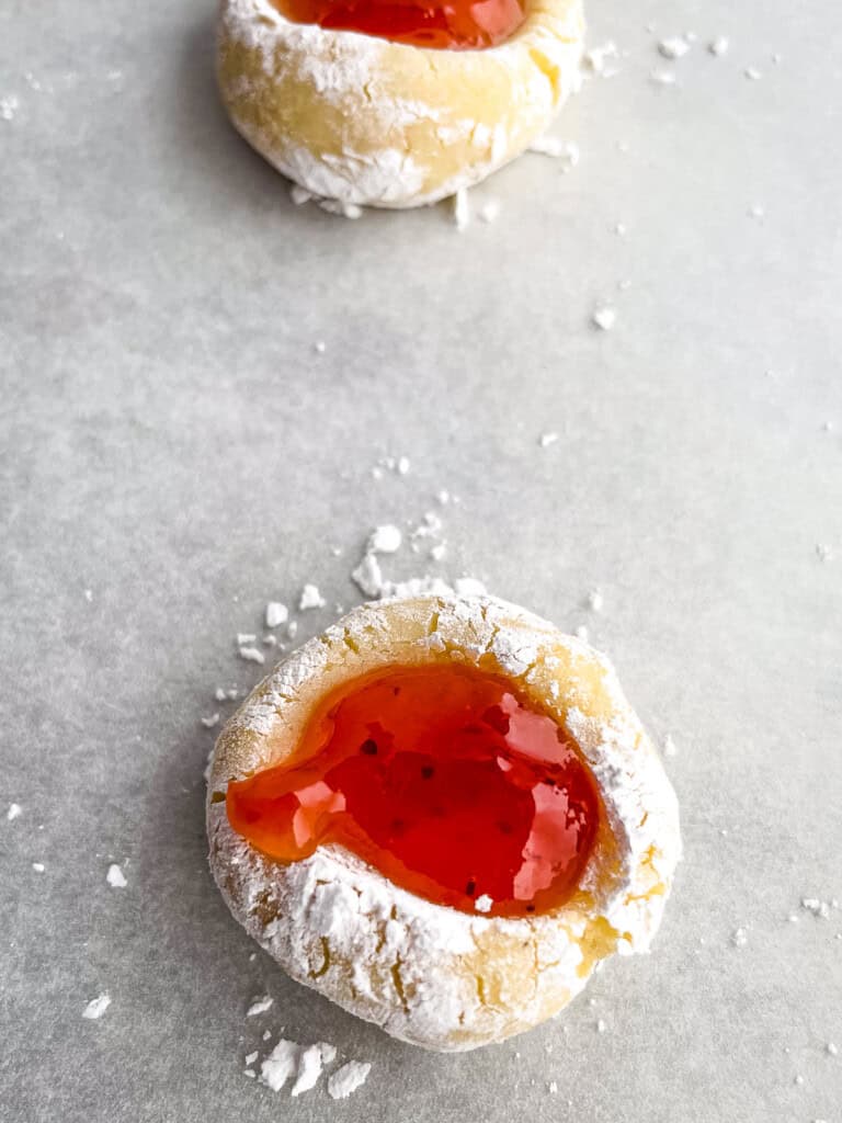 Gluten-free jam thumbprint dough rolled in powdered sugar and topped with jam on a baking sheet.