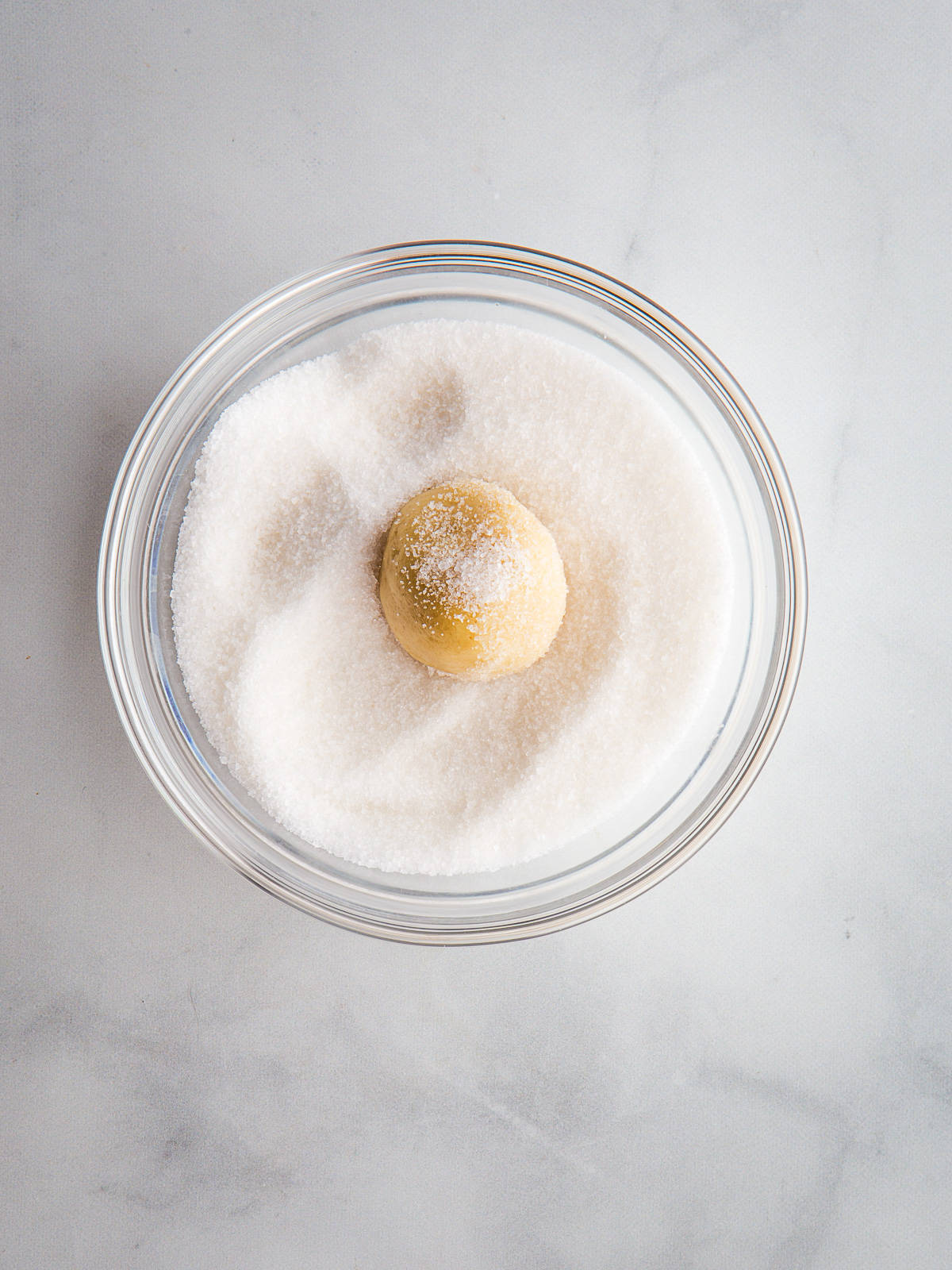 Gluten-Free sugar cookie dough ball in a bowl of sugar.