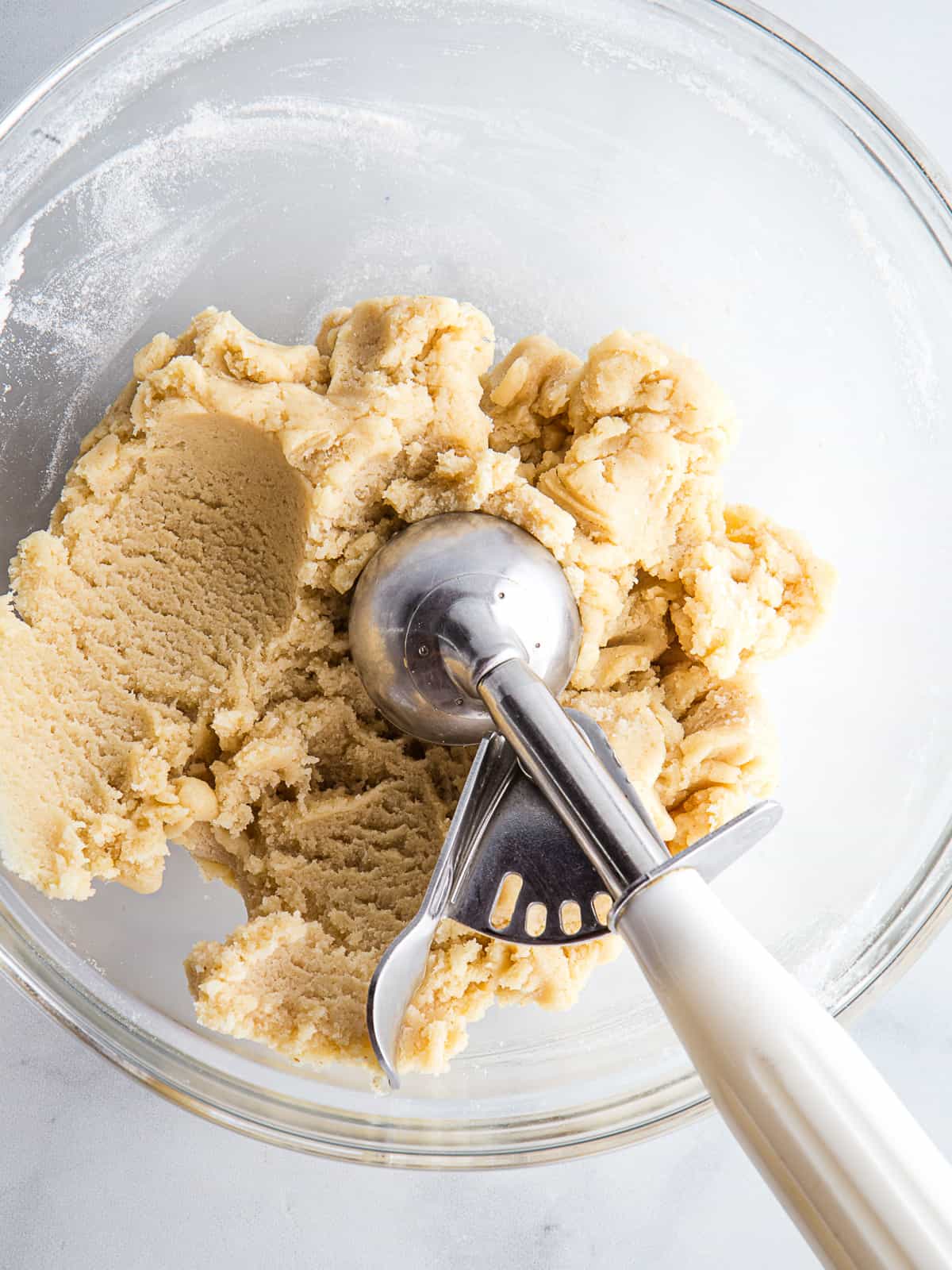 Gluten-free sugar cookie dough in a bowl with a cookie scoop.