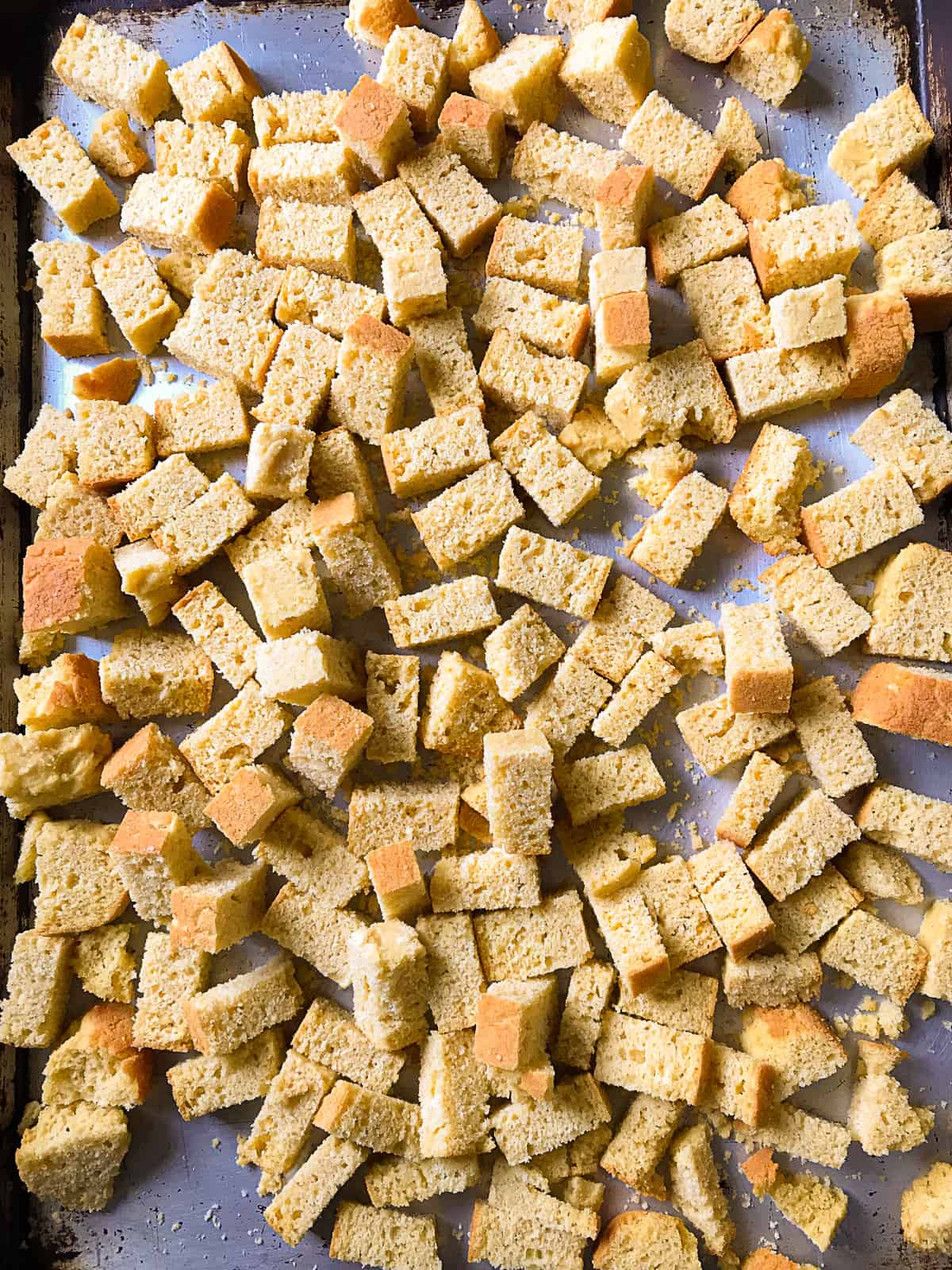 Cubed gluten-free cornbread for stuffing on a baking sheet.