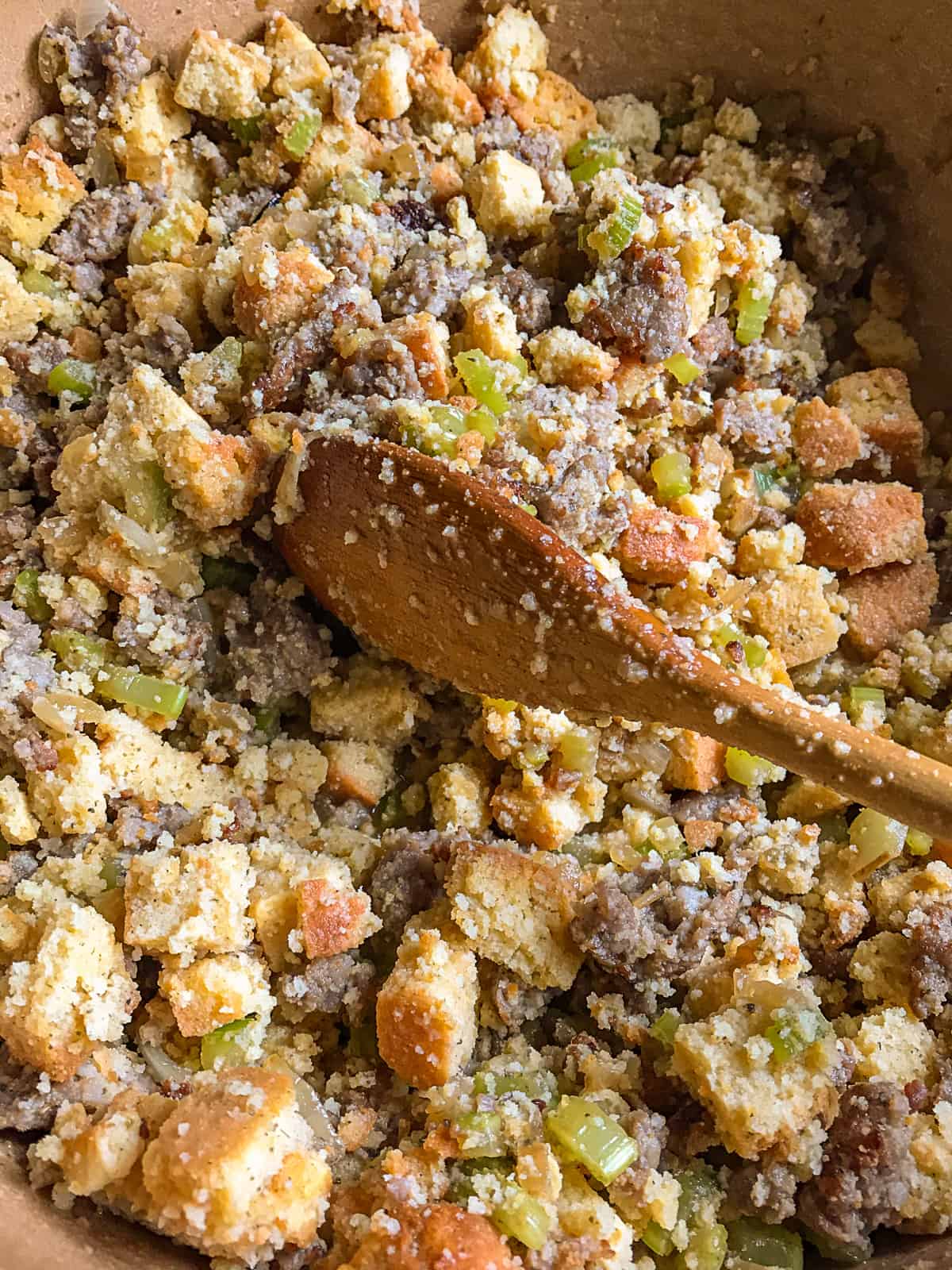 Gluten-free cornbread stuffing being mixed in a bowl with a wooden spoon.