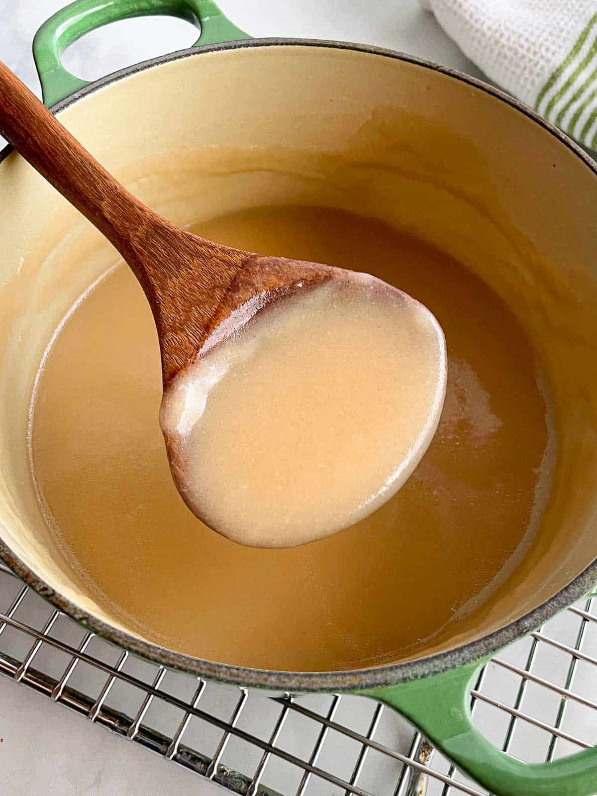 Homemade gluten-free gravy in a pan. A wooden spoon holds a spoonful of gravy above the pan.