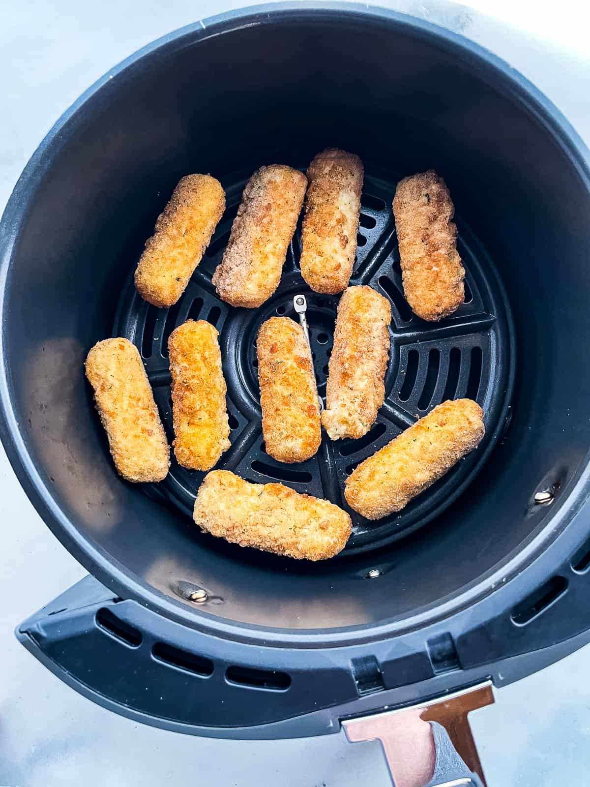 Gluten-free mozzarella sticks in an air fryer basket.