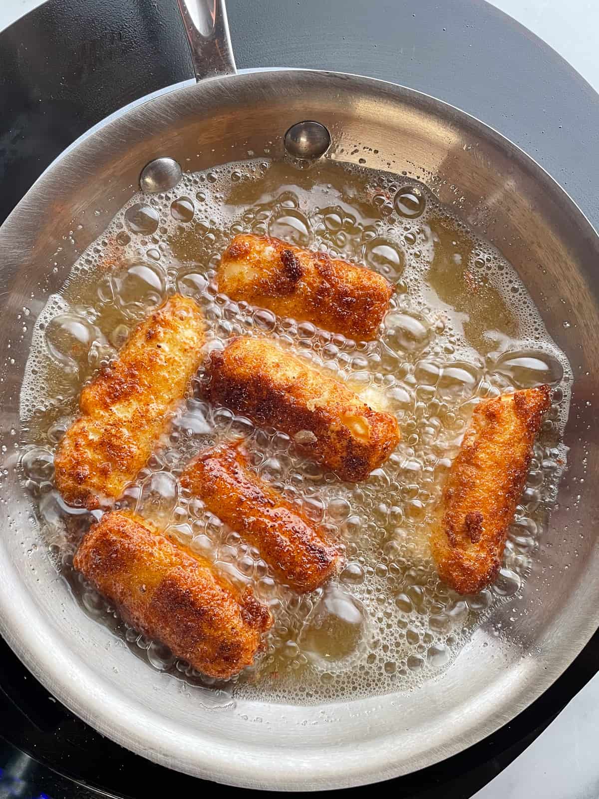 Gluten-free mozzarella sticks frying in a pan.
