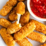 Gluten-free mozzarella sticks on a plate with a small bowl of tomato dipping sauce.