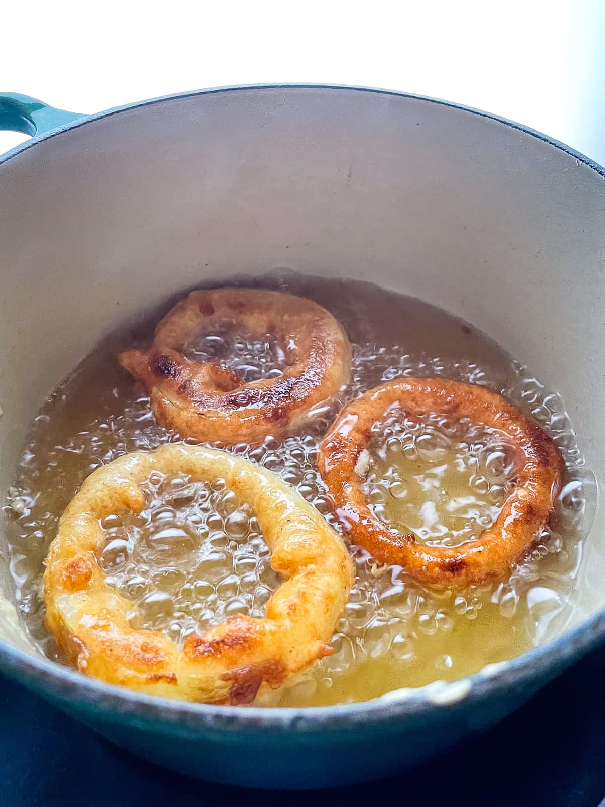Three onion rings frying in a pot of oil.