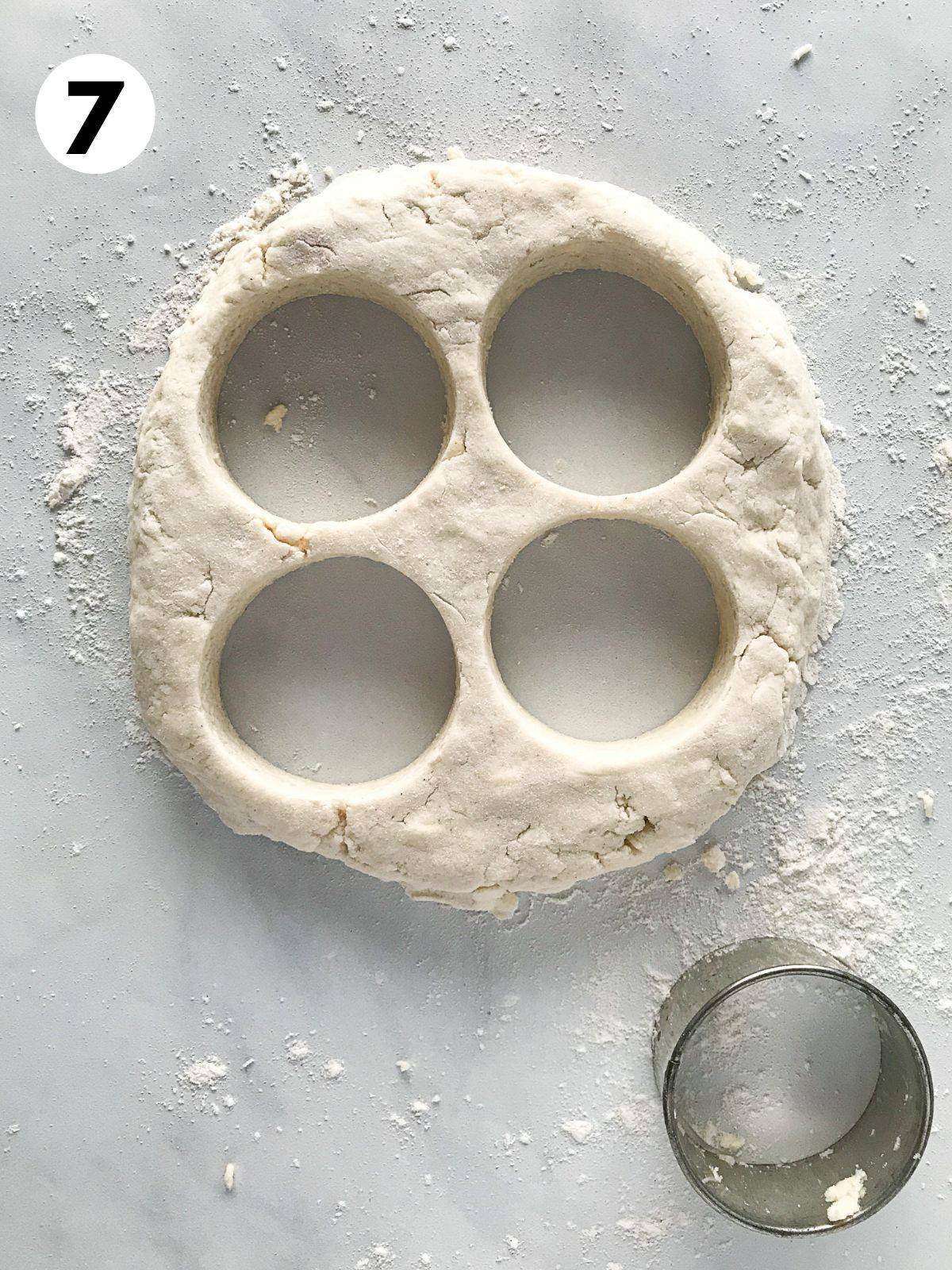 Gluten-free biscuit dough with four rounds cut out. A small 2-inch cutter sits off to the lower right side.