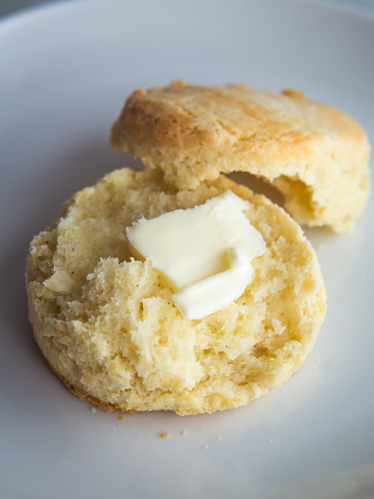 A gluten-free biscuit split in half topped with a pat of butter.