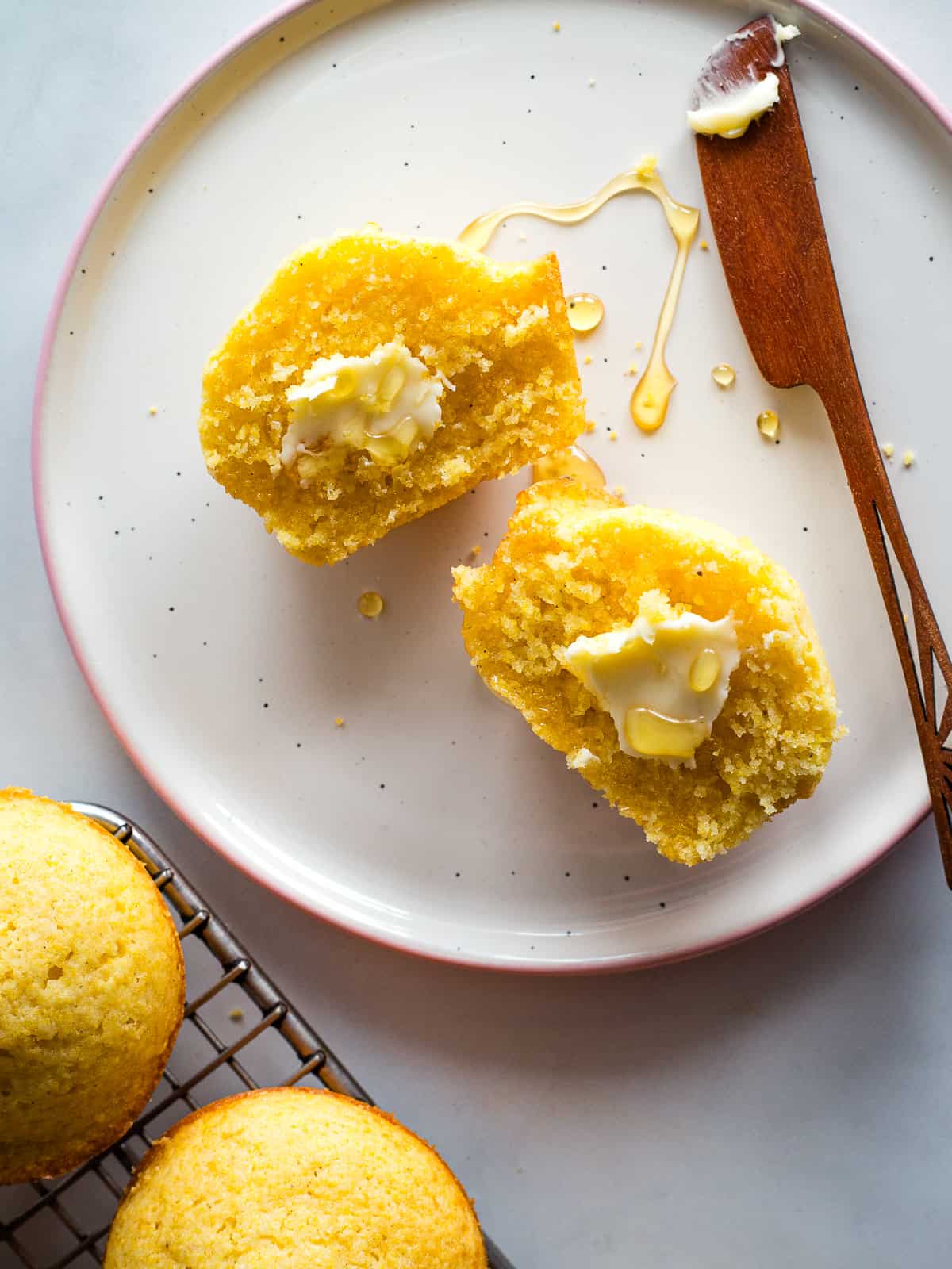 A gluten-free corn muffin split in half, spread with butter, and drizzled with honey.