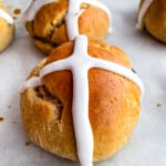 Gluten-free hot cross buns sitting on a baking sheet. The buns are piped with a white icing cross.