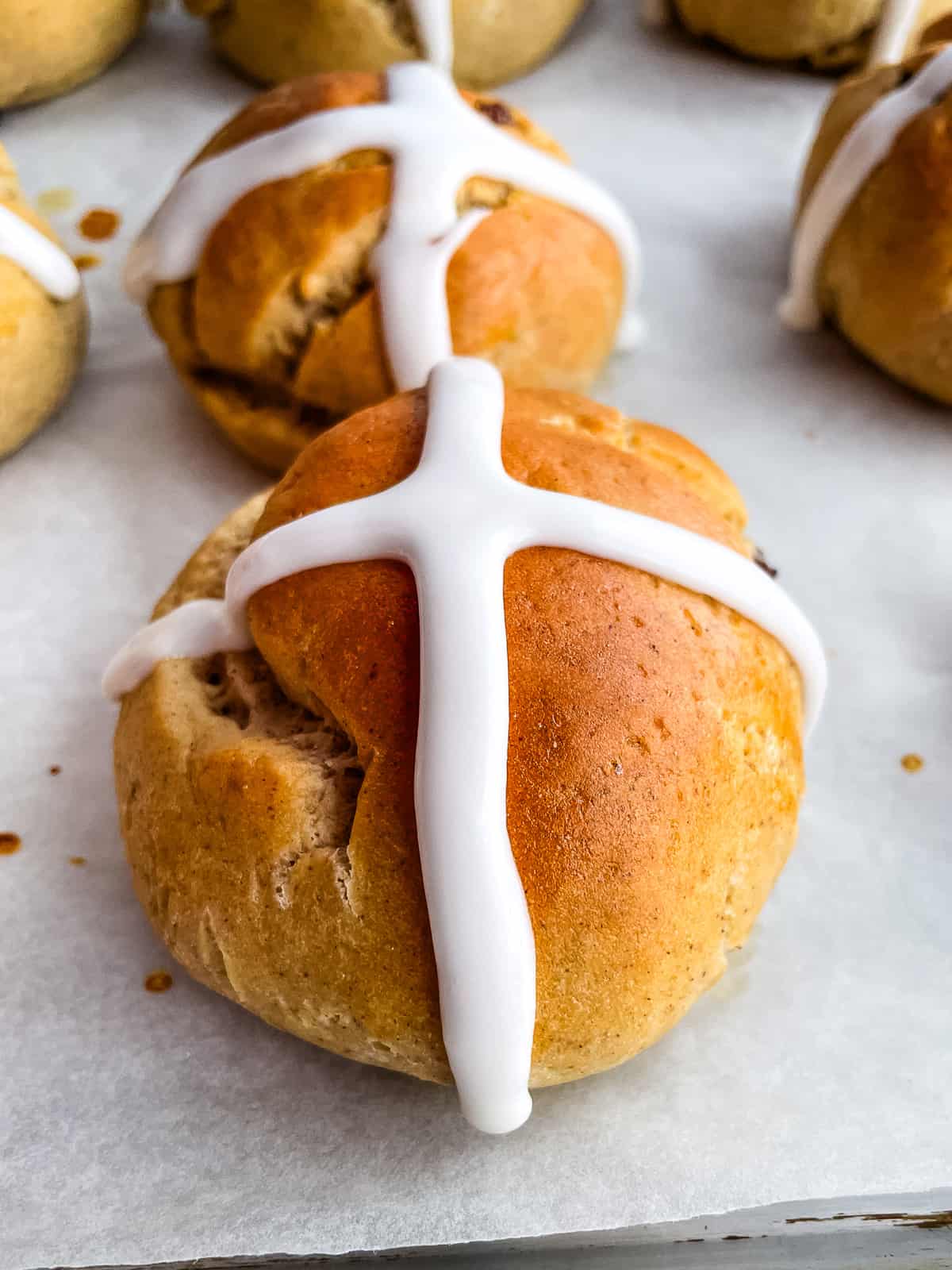 Gluten-free hot cross buns sitting on a baking sheet. The buns are piped with a white icing cross.