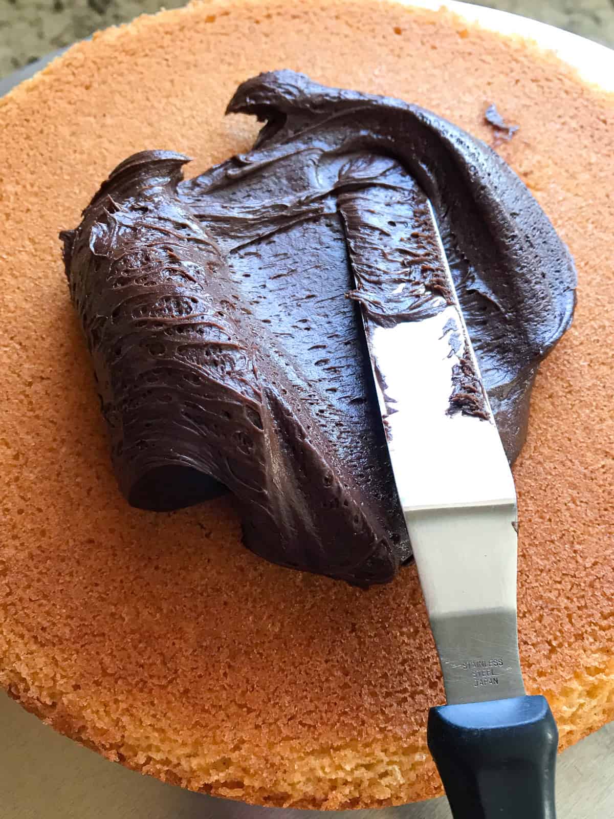 Spreading chocolate frosting on a gluten-free yellow cake round.
