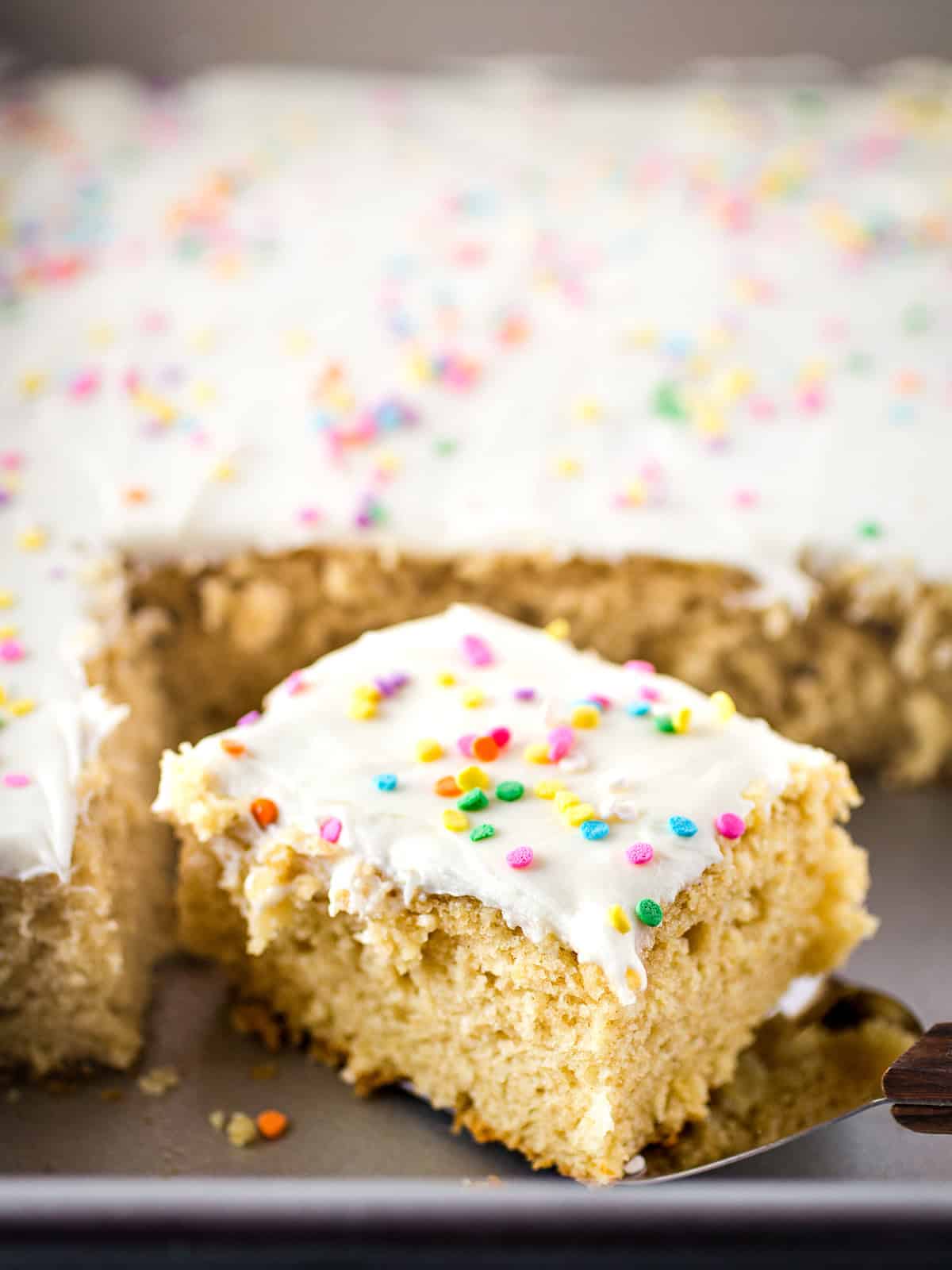 Gluten free vanilla sheet cake in the pan with frosting and sprinkles on top.