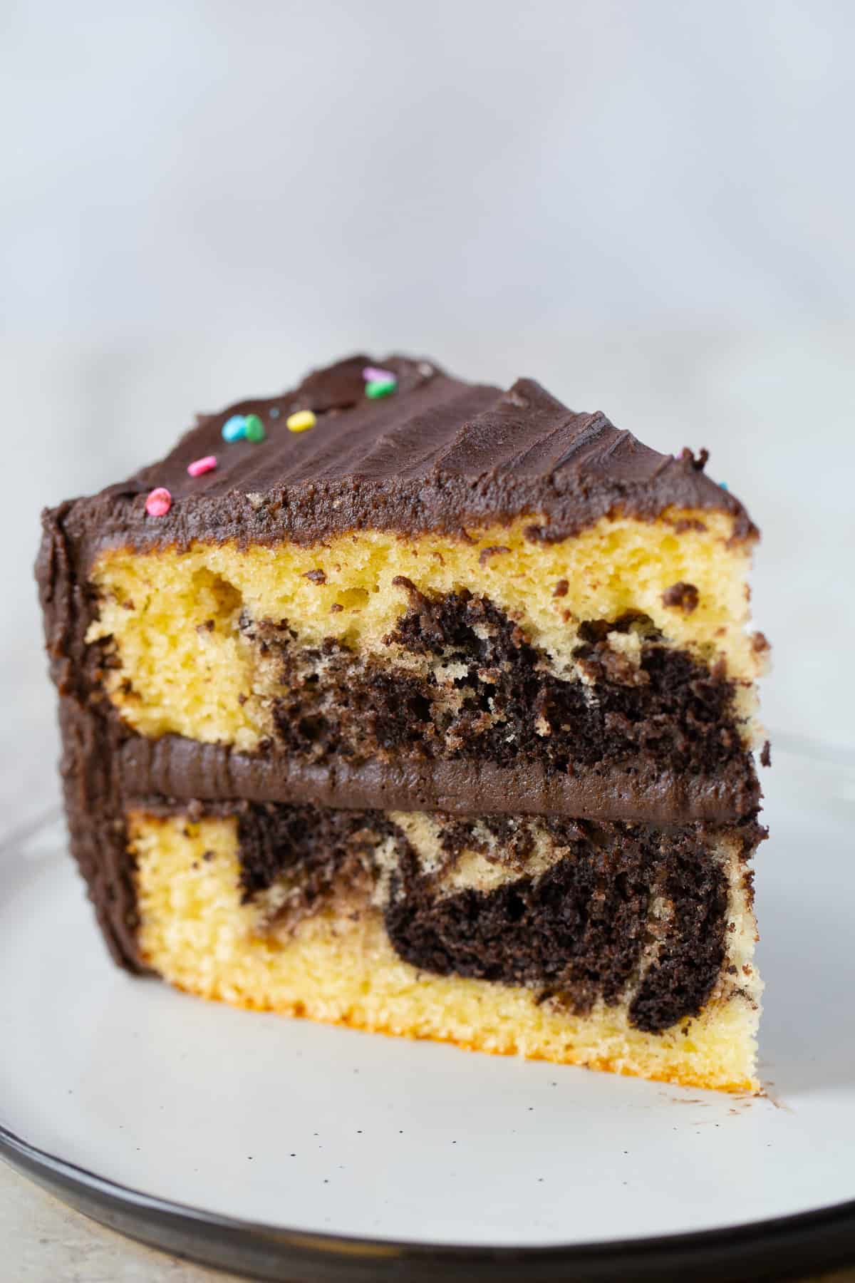 Slice of gluten-free marble cake on a plate. The cake is frosted with chocolate frosting.