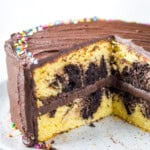 Gluten-free marble cake, frosted with chocolate frosting, on a cake plate. Two slices have been cut from the cake.