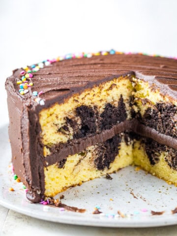 Gluten-free marble cake, frosted with chocolate frosting, on a cake plate. Two slices have been cut from the cake.