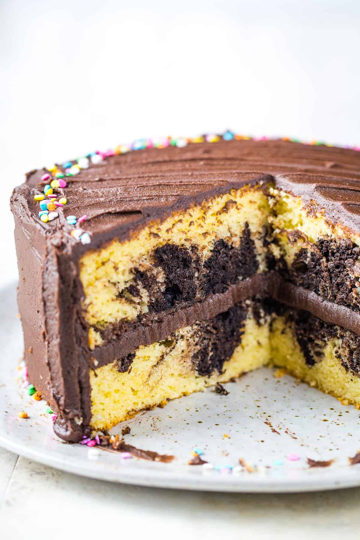 Gluten-free marble cake, frosted with chocolate frosting, on a cake plate. Two slices have been cut from the cake.