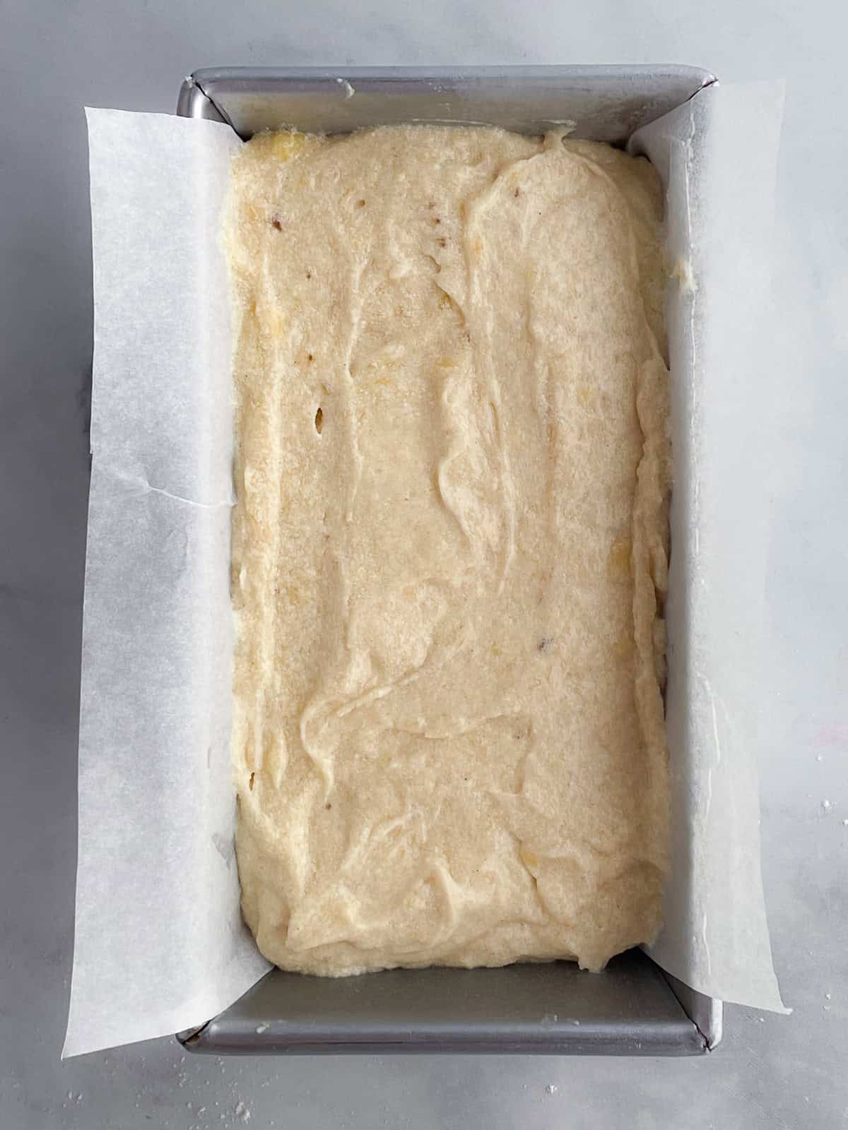 Gluten-free banana bread batter in a loaf pan that's been lined with parchment paper.