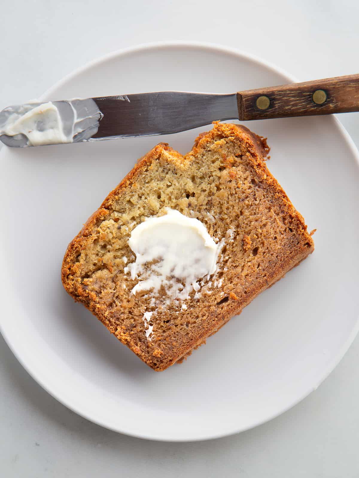 Gluten-free banana bread sliced on a plate spread with a little butter.