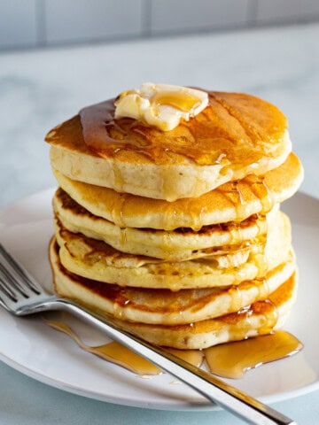 A stack of gluten-free pancakes topped with maple syrup and butter on a plate.