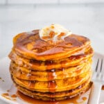 Stack of gluten-free pumpkin pancakes on a plate with butter and syrup.