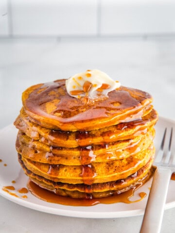 Stack of gluten-free pumpkin pancakes on a plate with butter and syrup.