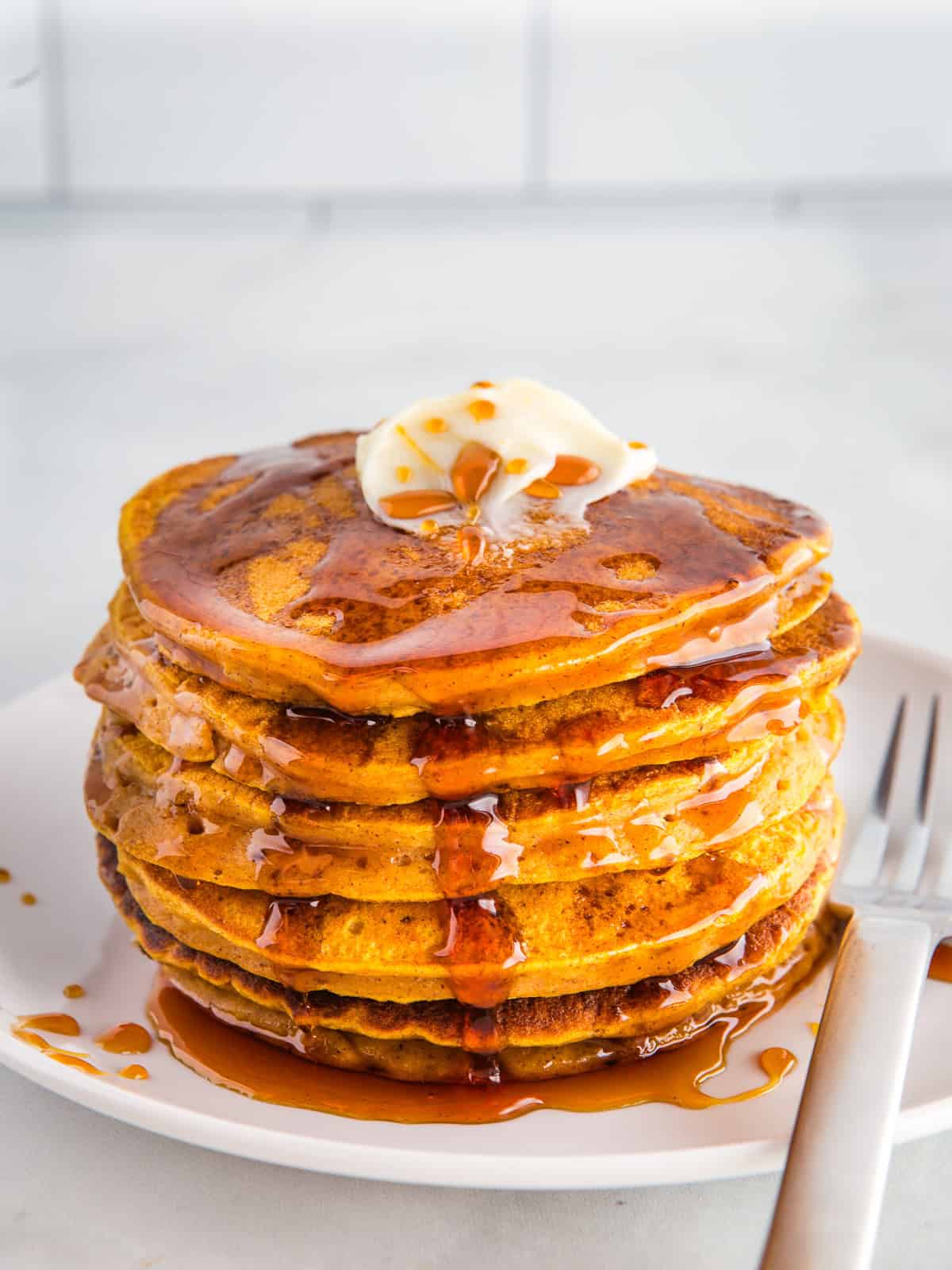 Stack of gluten-free pumpkin pancakes on a plate with butter and syrup.