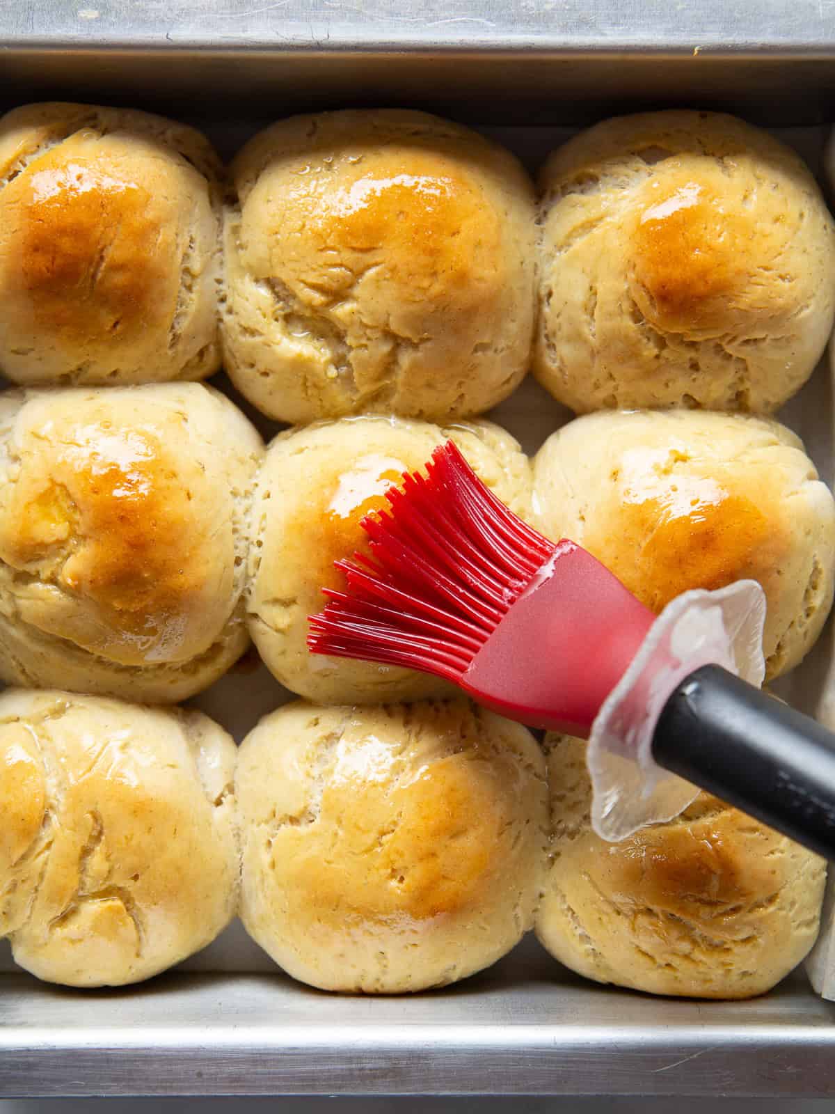 Brushing butter on gluten-free soft dinner rolls.