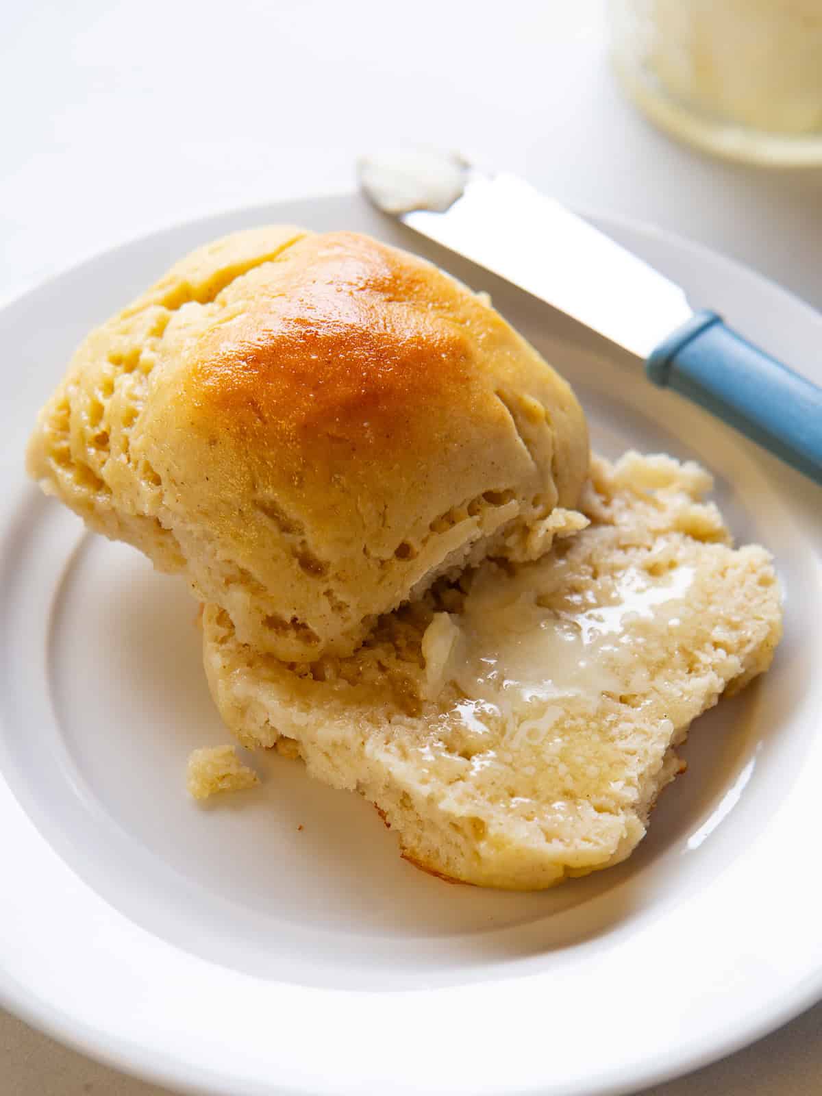 A gluten-free soft roll cut in half and spread with butter. The butter is melting on the warm roll.